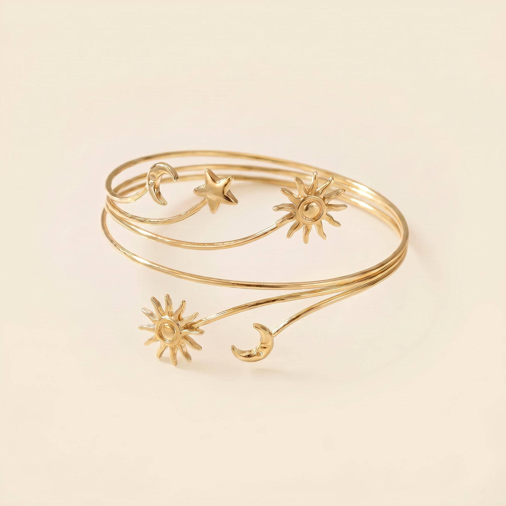 A delicate gold wrap bangle bracelet featuring celestial motifs including suns, moons, and a star, displayed on a warm cream background.