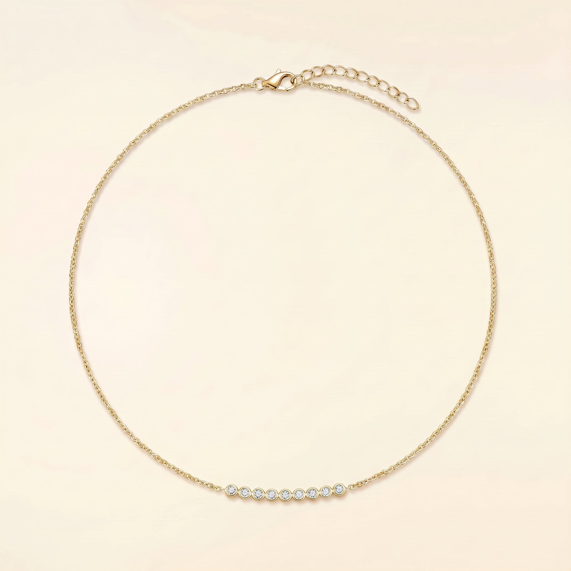 A delicate gold chain necklace with a small curved bar of clear round stones at the center, displayed on a light cream background.