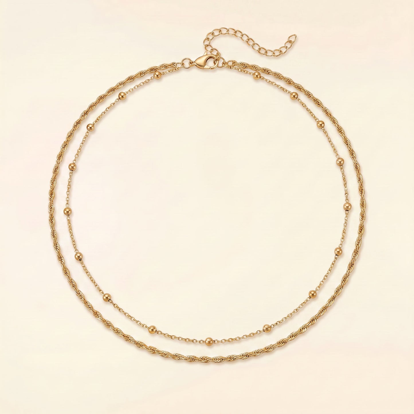 A double-strand gold chain necklace with small bead accents, displayed on a light cream background.