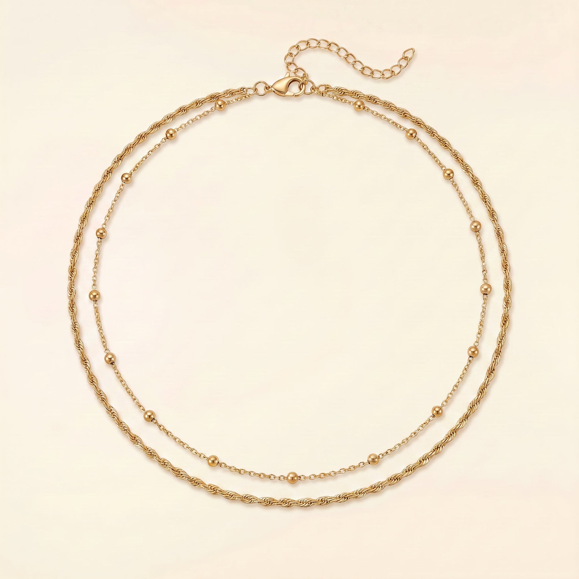 A double-strand gold chain necklace with small bead accents, displayed on a light cream background.