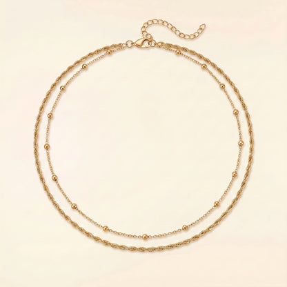 A double-strand gold chain necklace with small bead accents, displayed on a light cream background.