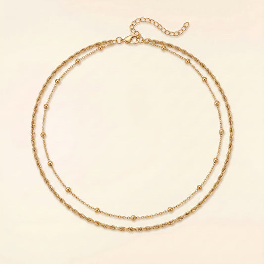 A double-strand gold chain necklace with small bead accents, displayed on a light cream background.