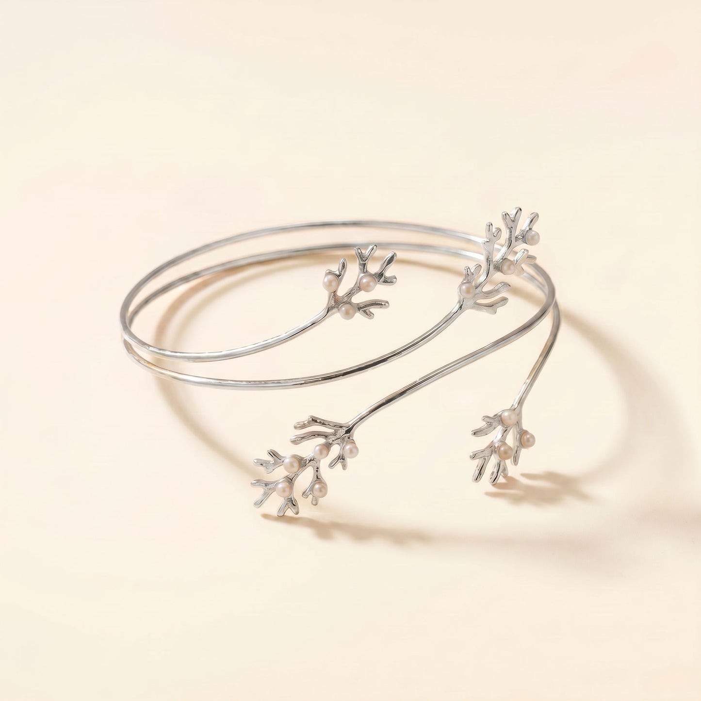 A delicate silver open cuff bangle featuring three small branching coral or branch-like motifs, photographed on a warm cream background.
