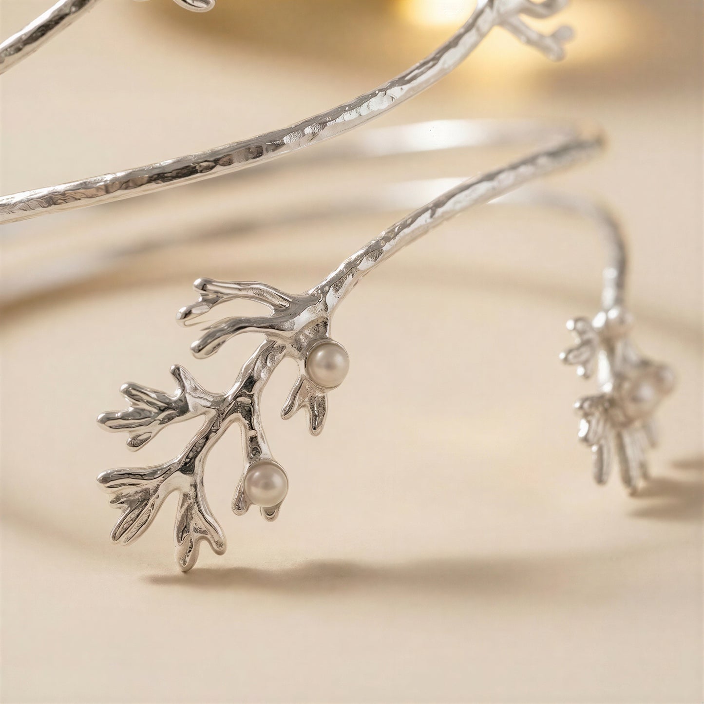 A close-up of a silver bangle bracelet designed to look like a branch with small pearl-like beads, photographed on a soft beige background.