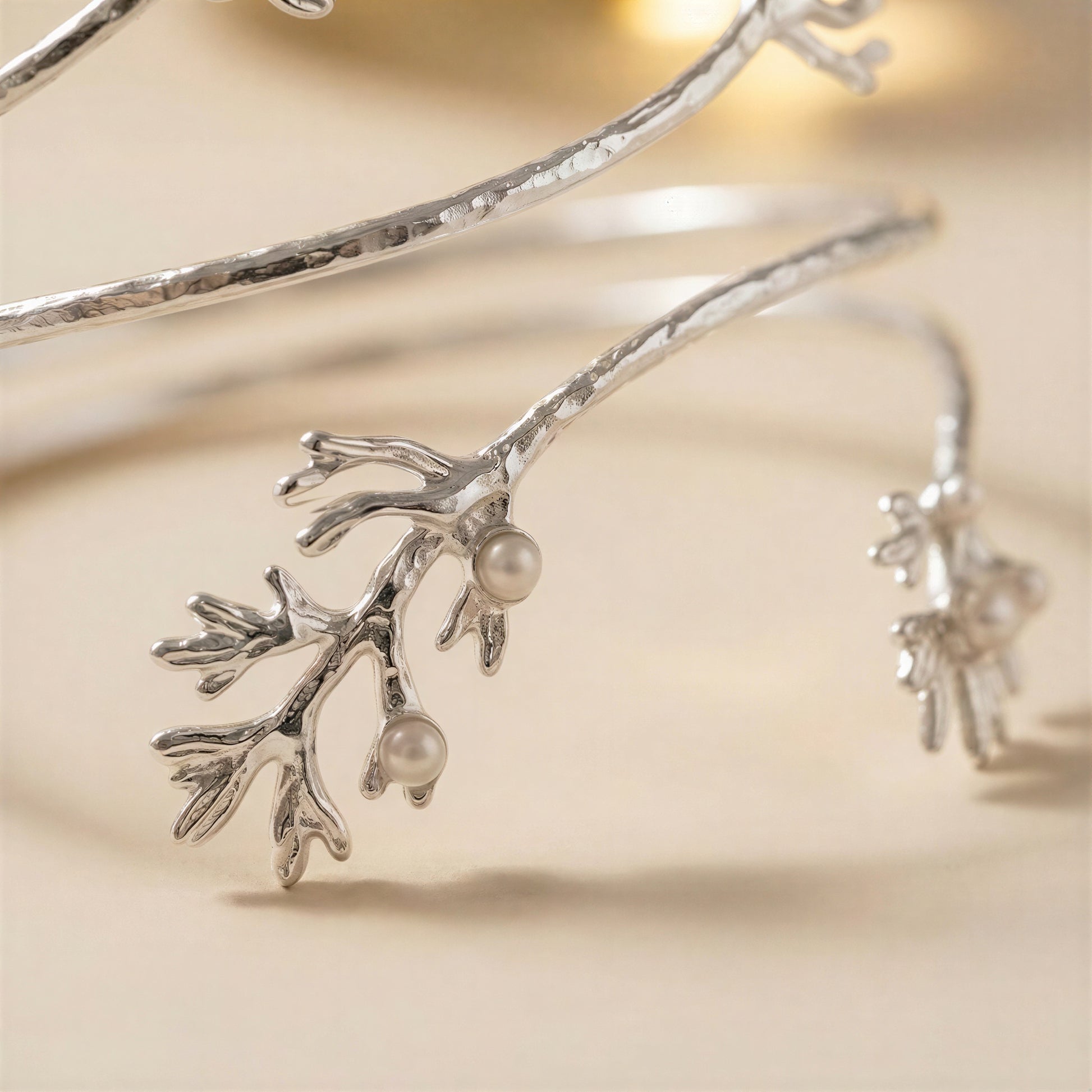 A close-up of a silver bangle bracelet designed to look like a branch with small pearl-like beads, photographed on a soft beige background.
