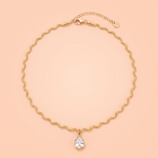 Onda Choker in gold laid flat on a peach background