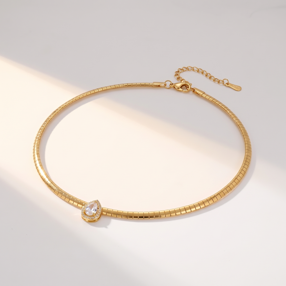 Aura Choker in gold on a white surface in soft sunlight