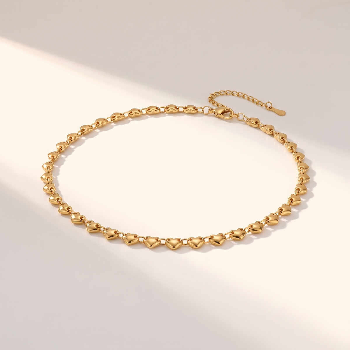 Cuori Choker in gold on a white surface in soft sunlight