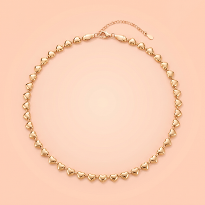 Cuori Choker in gold laid flat on a peach background