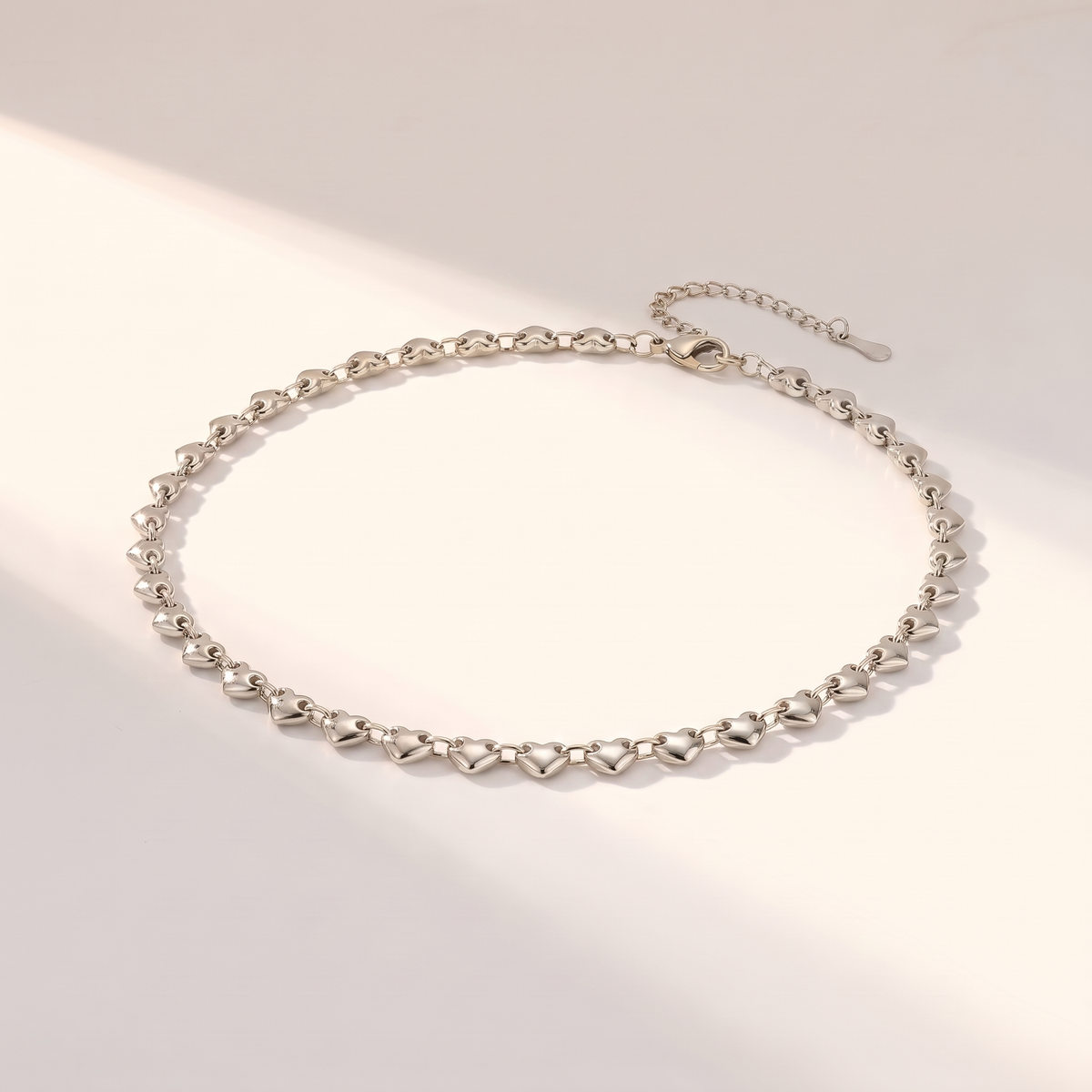 Cuori Choker in silver on a white surface in soft sunlight