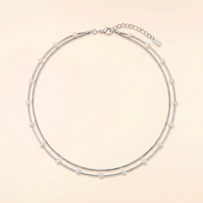 A double-strand silver chain necklace adorned with small white pearls, displayed on a light beige background.