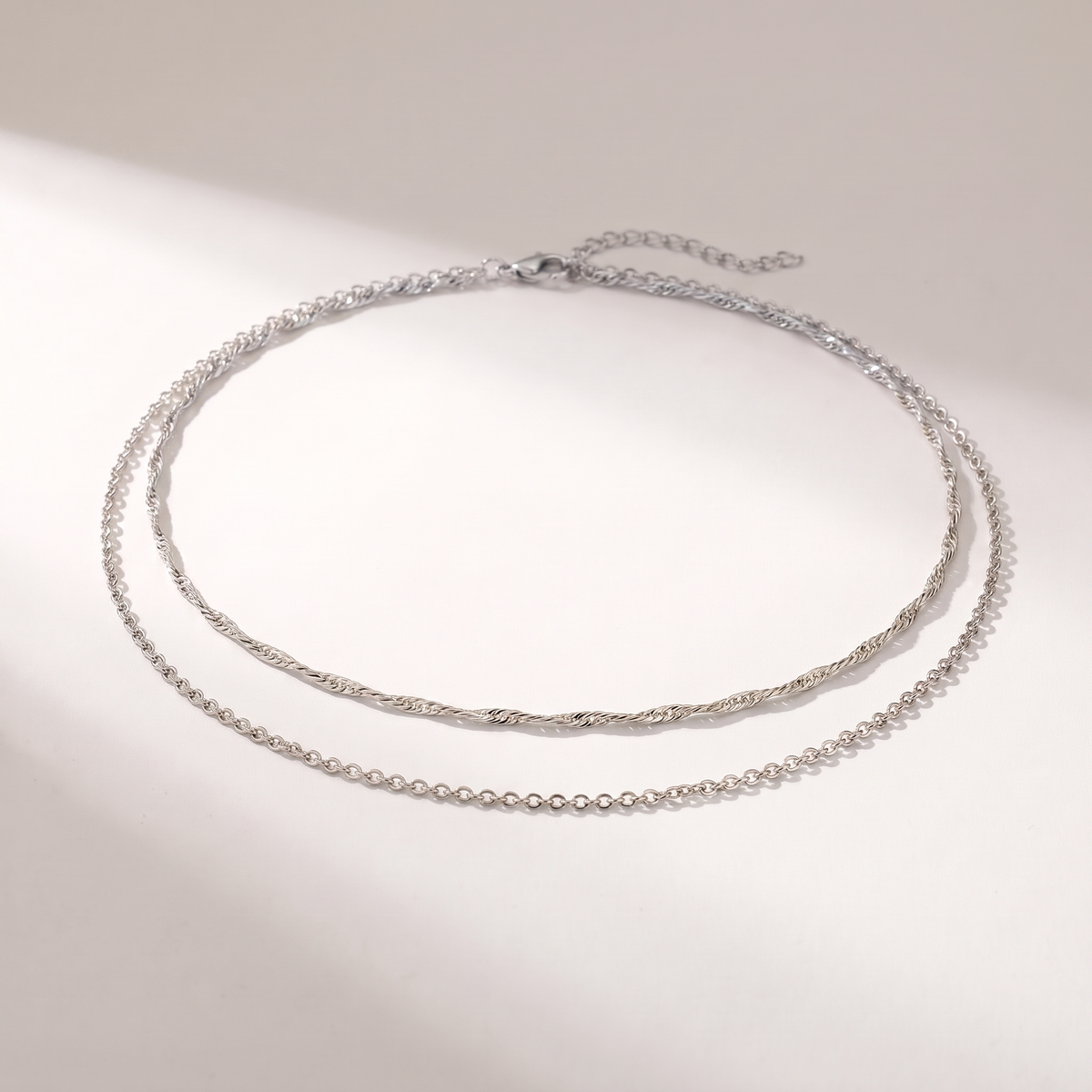 A delicate silver double-layer necklace with a twisted top chain and a fine beaded bottom chain, displayed on a clean white surface with soft shadows.