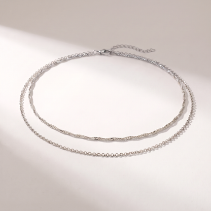 A delicate silver double-layer necklace with a twisted top chain and a fine beaded bottom chain, displayed on a clean white surface with soft shadows.