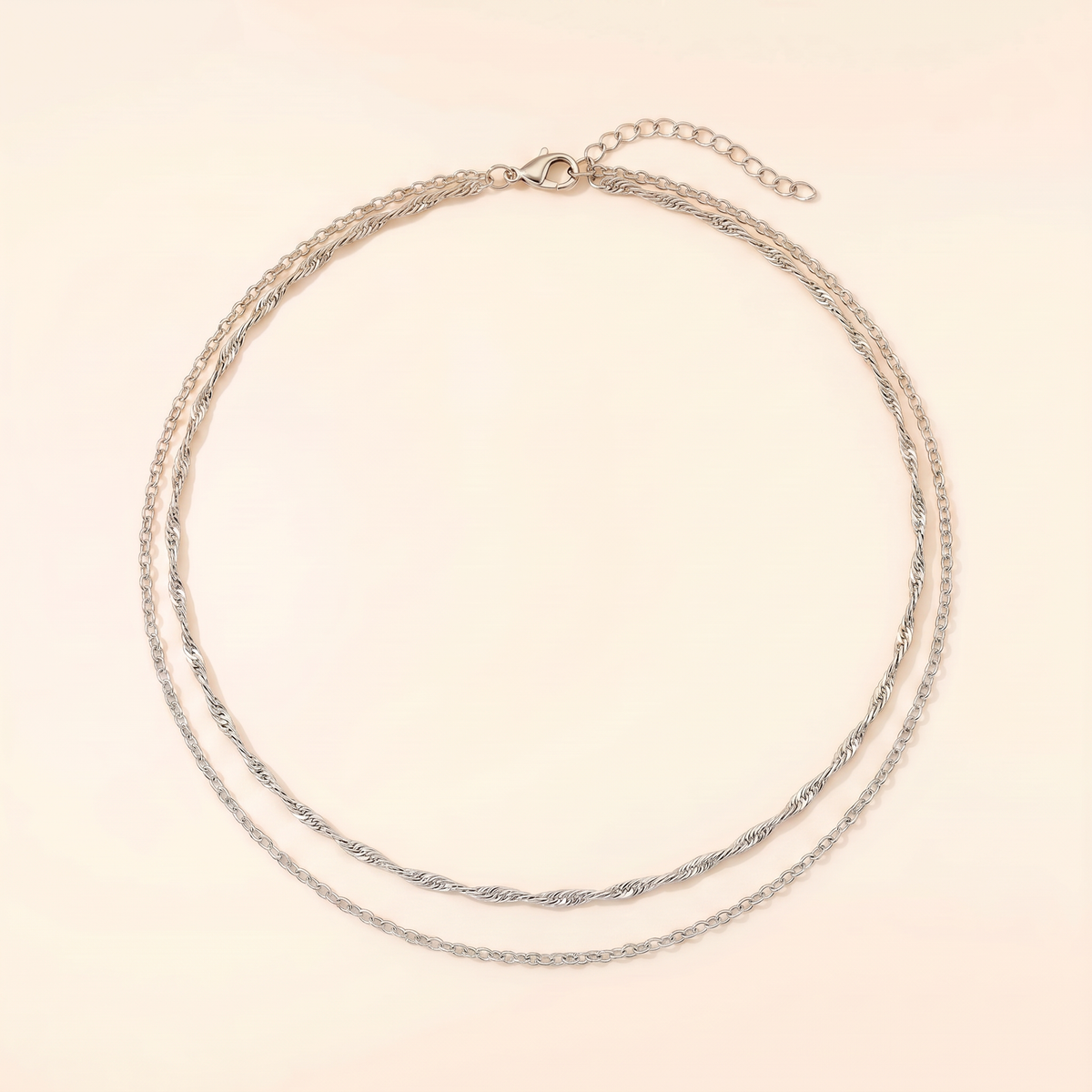 A delicate double-layered silver chain necklace with a small lobster clasp and extender chain, displayed on a light cream background.