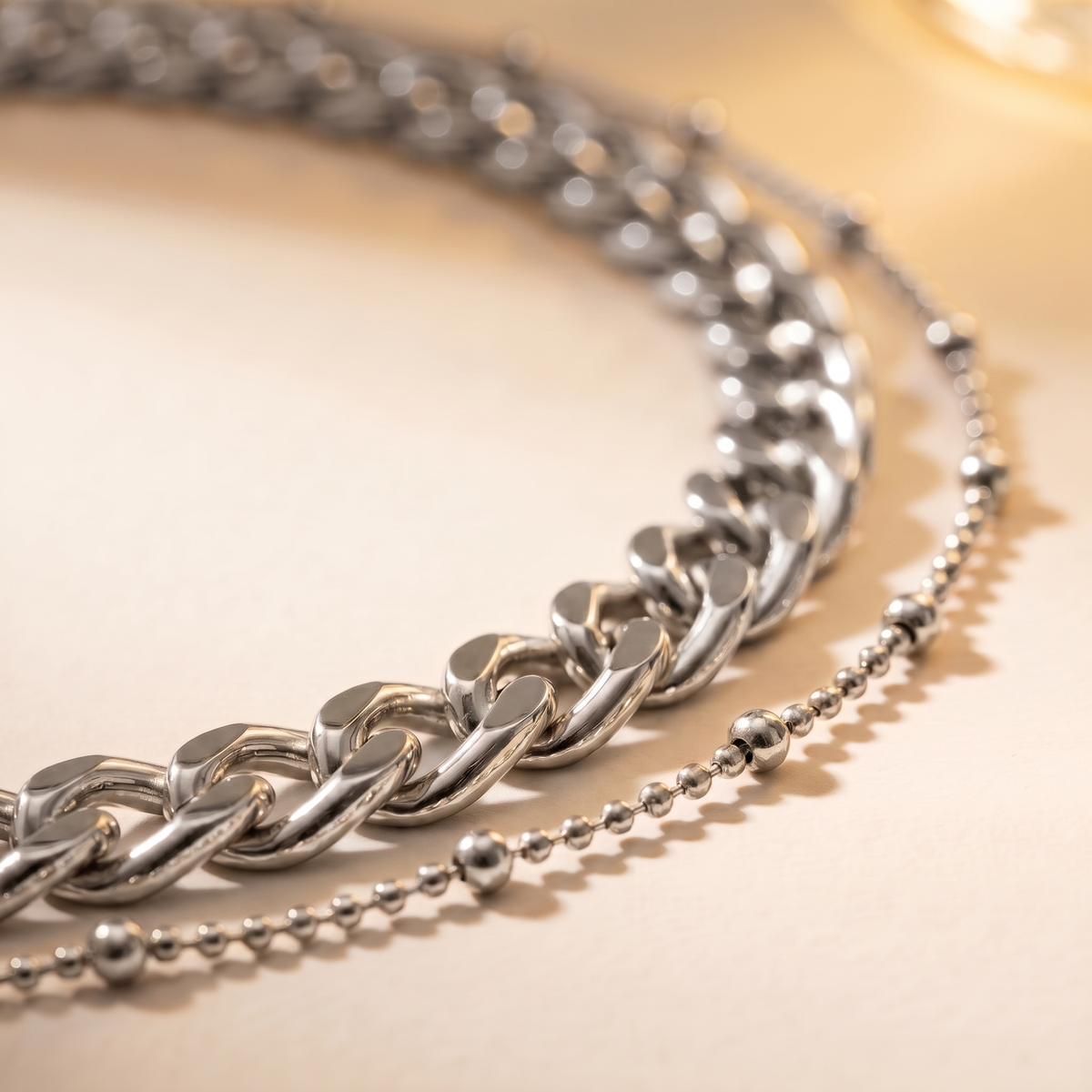 A silver-toned double-layer necklace featuring a chunky curb chain and a delicate beaded chain, displayed on a light cream background.