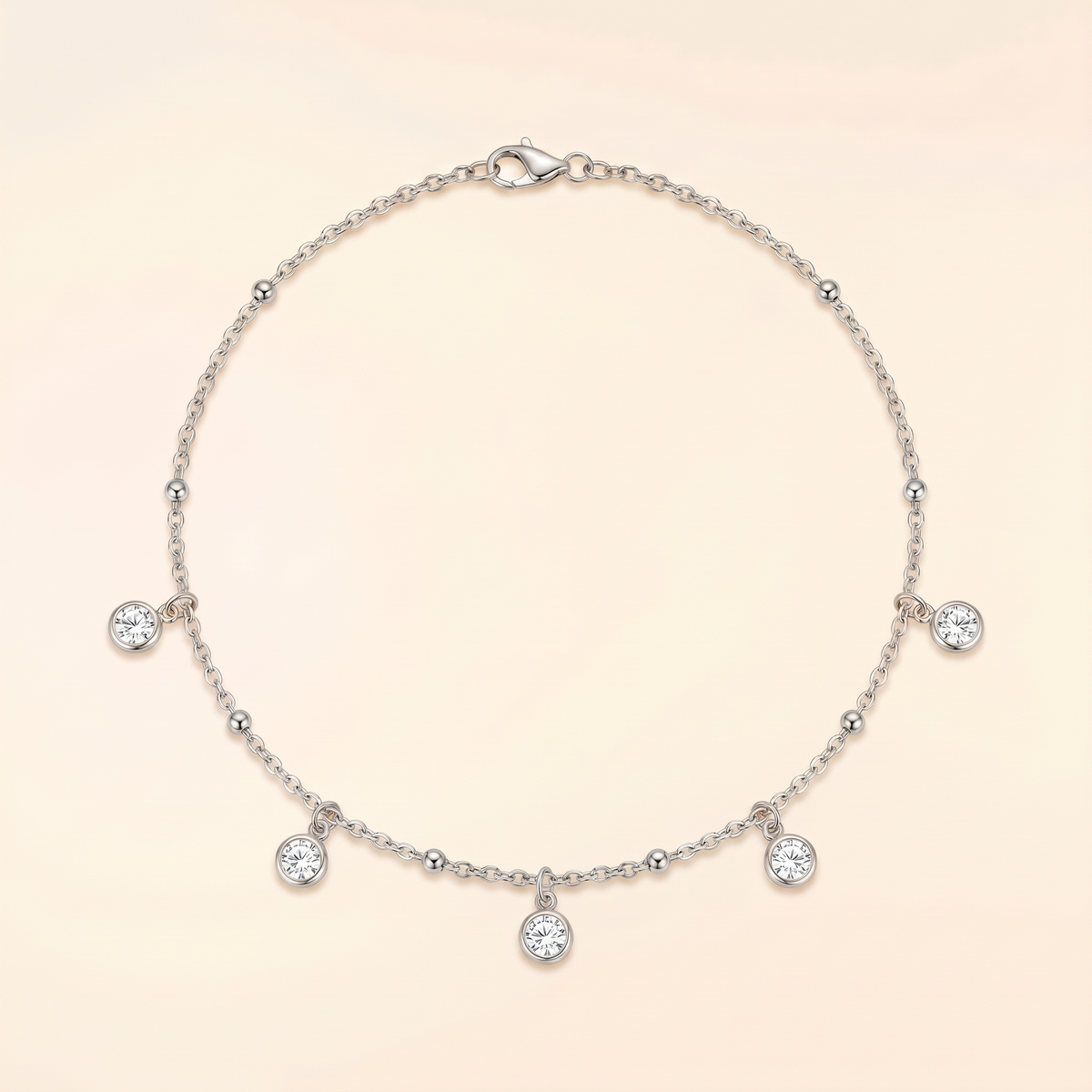 A delicate silver chain necklace with five small clear gemstone charms and a lobster clasp, displayed on a soft cream background.