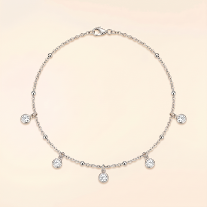 A delicate silver chain necklace with five small clear gemstone charms and a lobster clasp, displayed on a soft cream background.