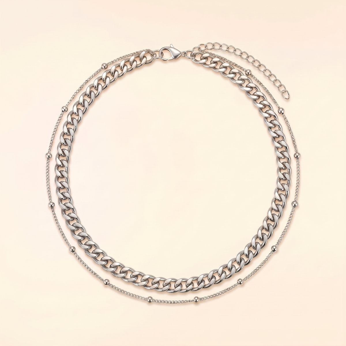 A silver-toned double-layer necklace featuring a chunky curb chain and a delicate beaded chain, displayed on a light cream background.