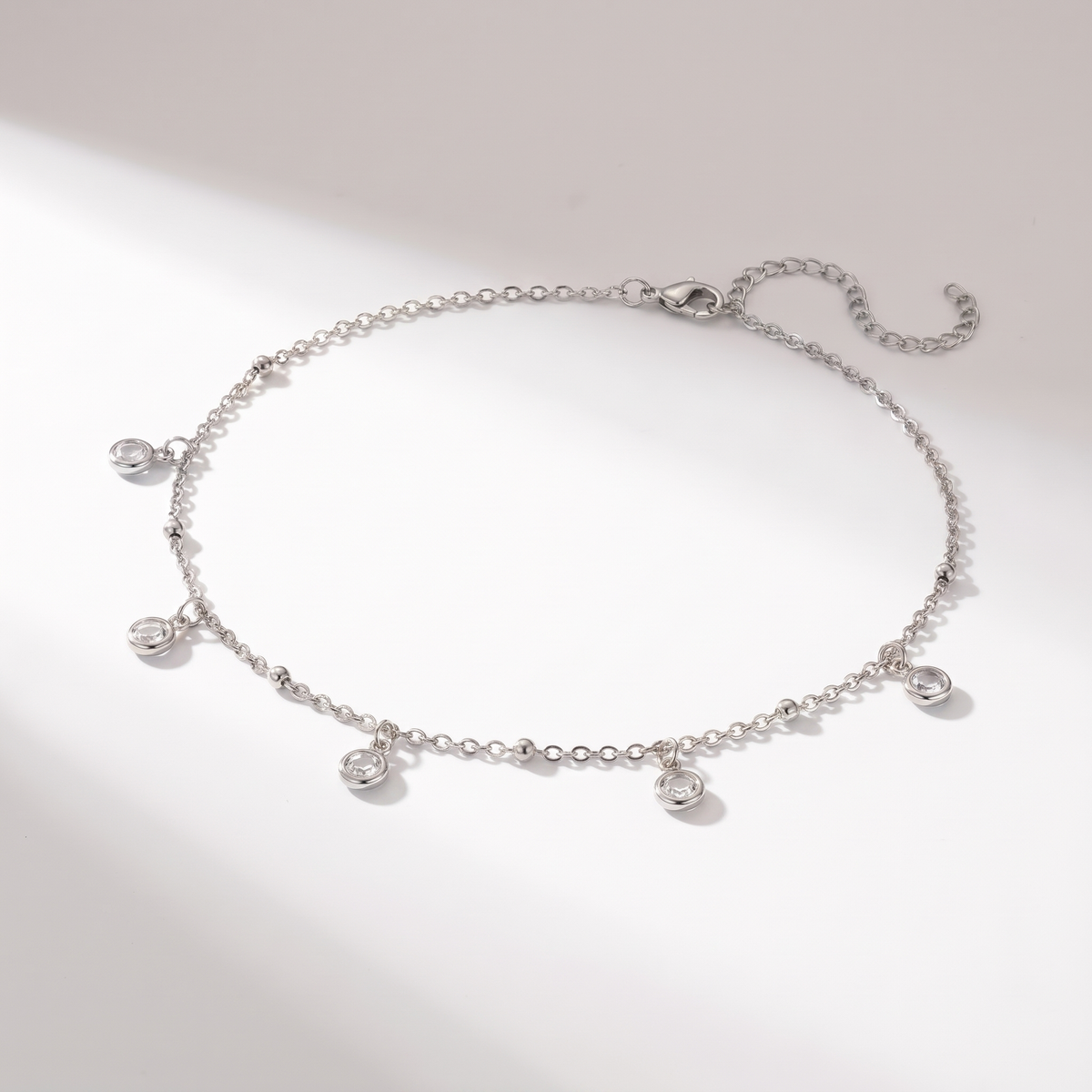 A delicate silver chain necklace with five small clear gemstone charms, displayed on a clean white background with soft shadows.