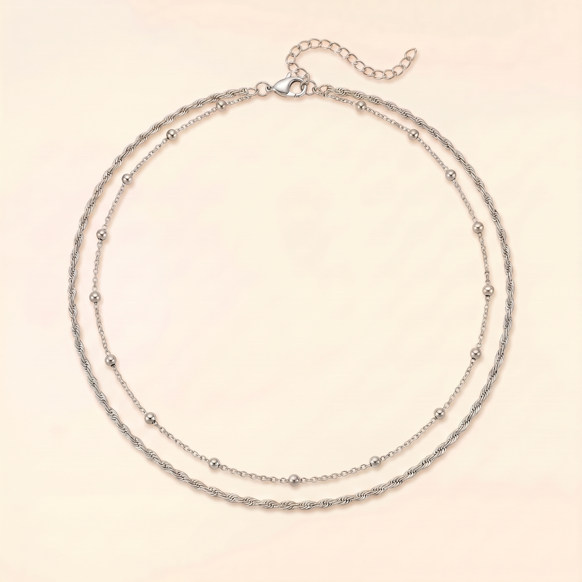A double-strand silver chain necklace with small bead accents, displayed on a light cream background.