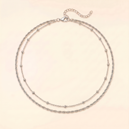 A double-strand silver chain necklace with small bead accents, displayed on a light cream background.