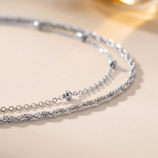 A double-strand silver chain necklace with small bead accents, displayed on a light cream background.