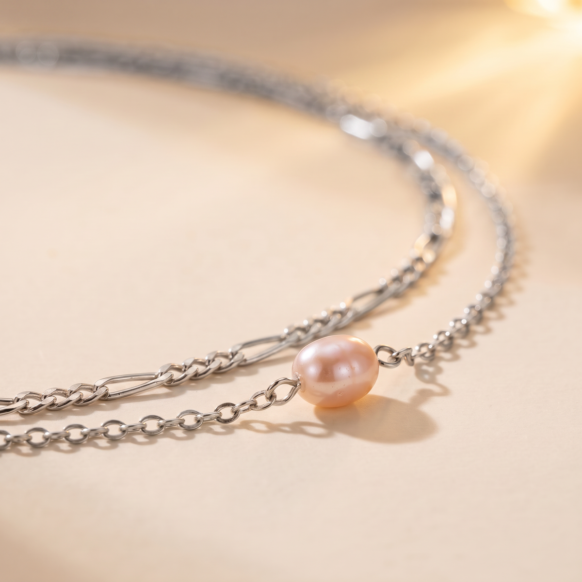 A delicate silver chain necklace featuring a single lustrous pearl pendant, photographed on a warm beige background with soft sunlight and shadows.
